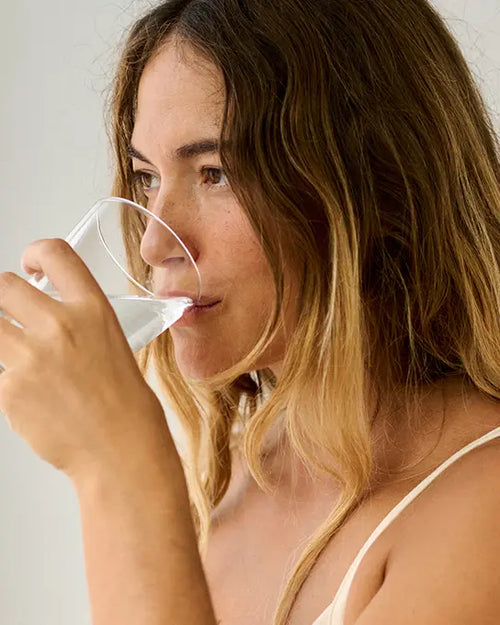 Femme tenant une gélule de complément alimentaire avec un verre d'eau