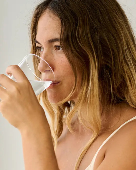 Femme tenant une gélule de complément alimentaire avec un verre d'eau