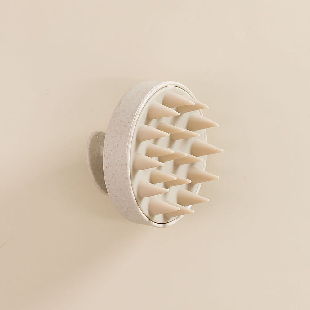 Spazzola in silicone per il cuoio capelluto, vista laterale, posata su una superficie. 

