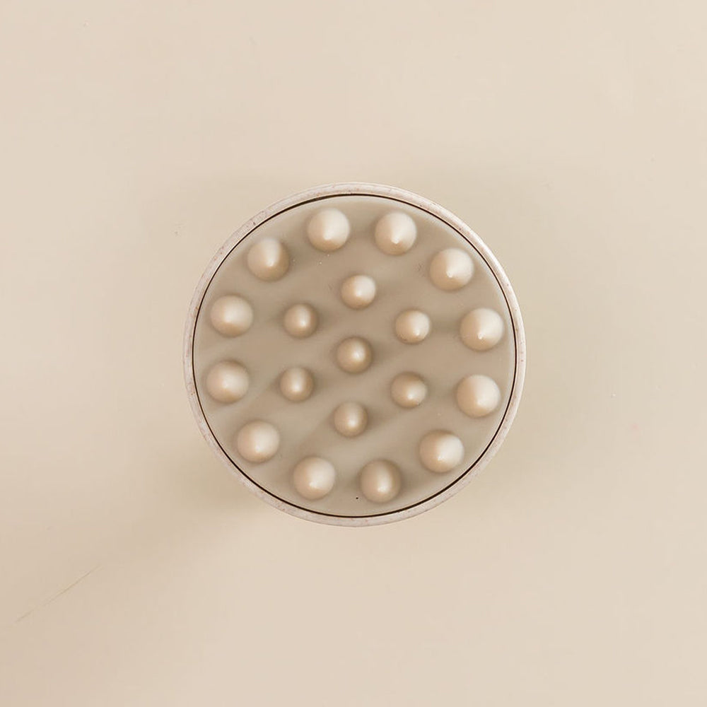 Spazzola con punte in silicone per il cuoio capelluto, vista dall'alto, posata su una superficie.







